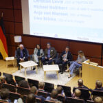 Diskussionsrunde auf einer Konferenz, fünf Personen auf der Bühne, Publikum im Saal, Fahnen von Schweden, EU und Deutschland.